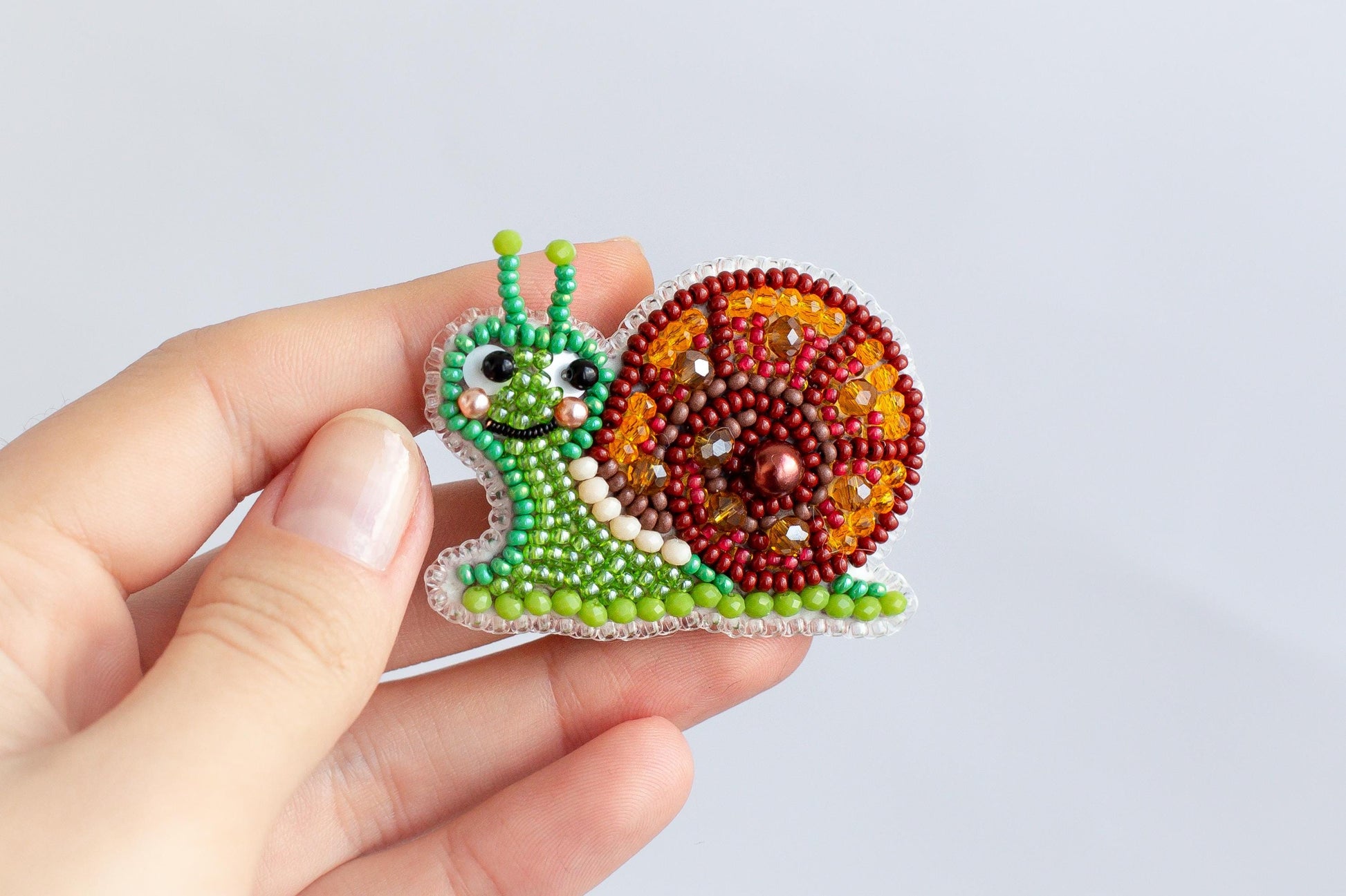 A hand holding a colorful, beaded snail-shaped object against a plain background.