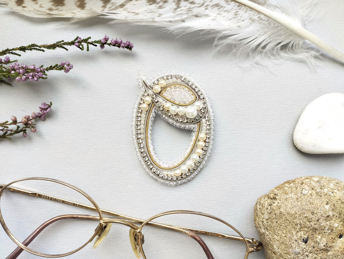 a close-up view of a pair of glasses, a decorative brooch, and various natural elements such as feathers, stones, and flowers.