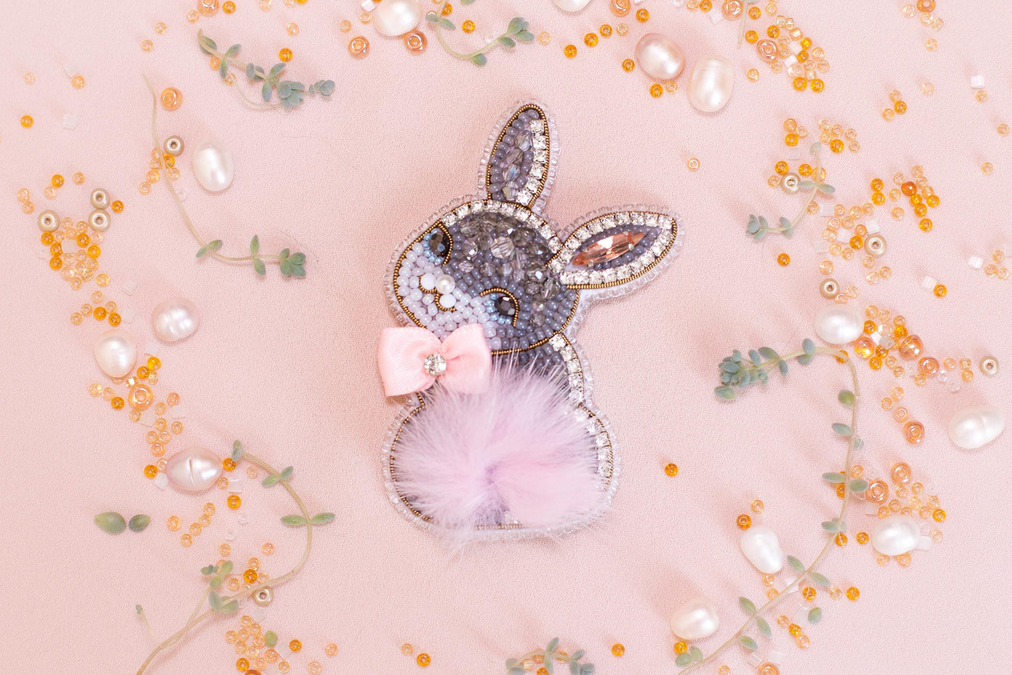 a decorative Easter bunny charm adorned with rhinestones and pearls, surrounded by scattered beads and sequins in shades of pink and gold.