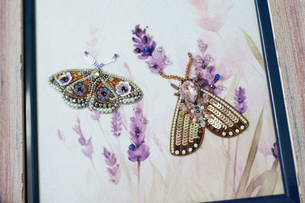 two intricately designed butterflies, one with a metallic and the other with a floral motif, set against a background of purple flowers.