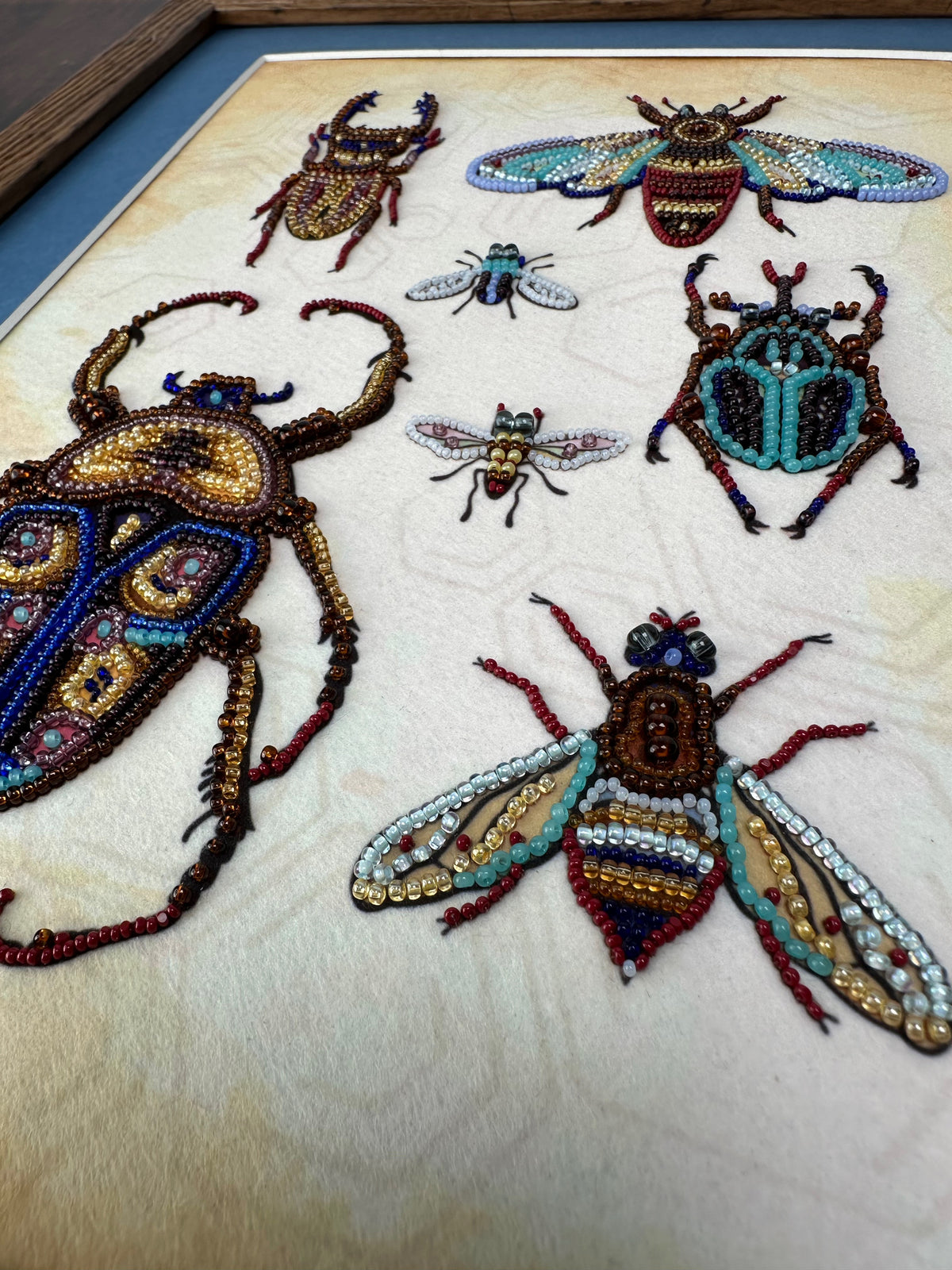 a collection of intricately designed insects, including a large beetle, a smaller bee, and several other insects, all meticulously crafted using colorful beads and threads.
