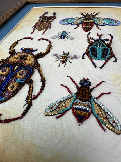 a collection of intricately designed insects, including a large beetle, a smaller bee, and several other insects, all meticulously crafted using colorful beads and threads.