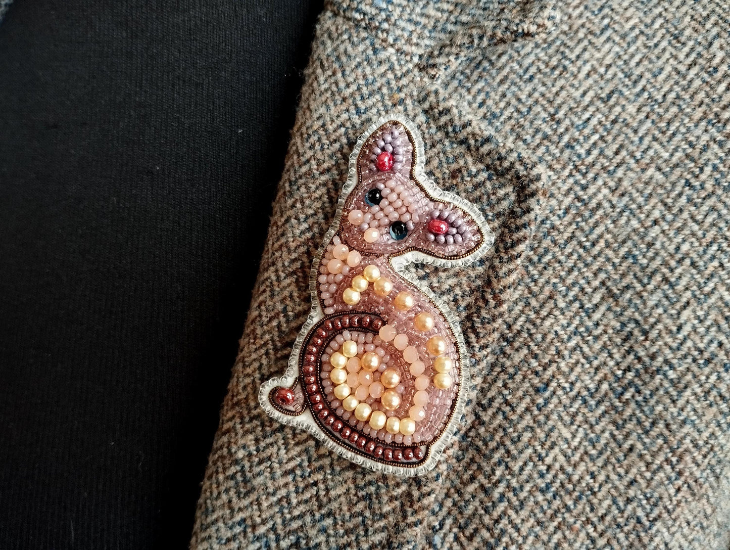 a close-up view of a cat-shaped embroidered patch on a fabric, with a dark background.