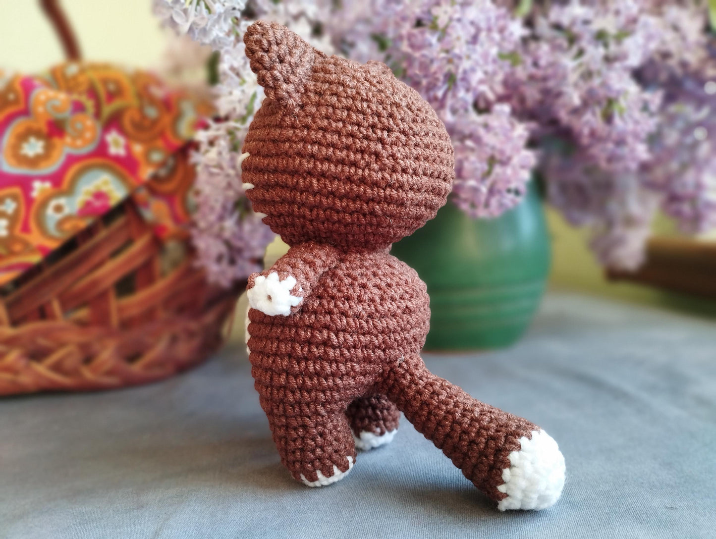 a crocheted teddy bear sitting next to a basket of flowers