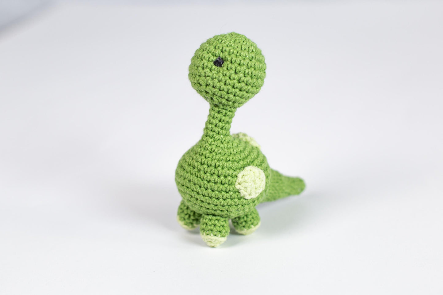 a crocheted green toy dinosaur on a white background