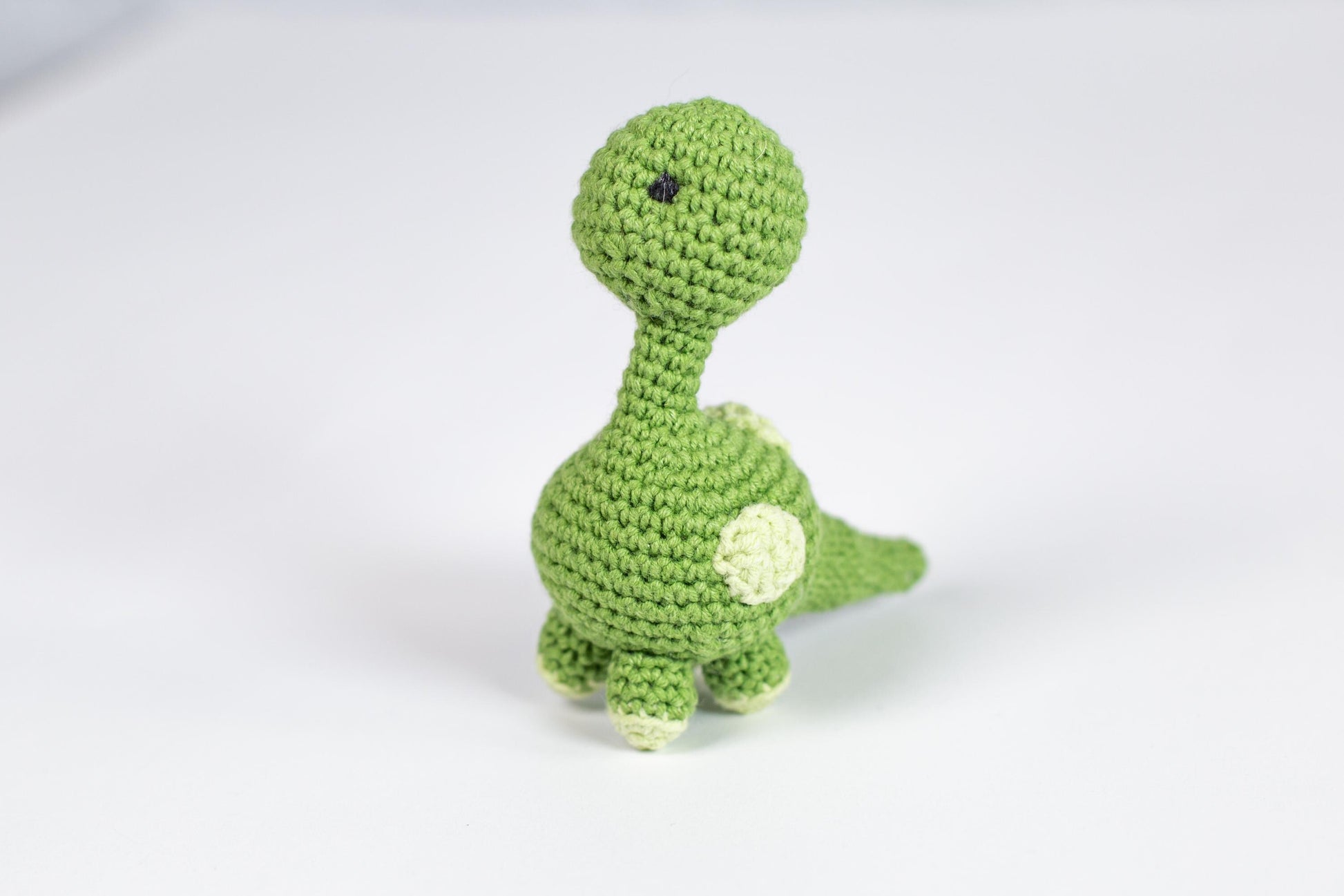 a crocheted green toy dinosaur on a white background