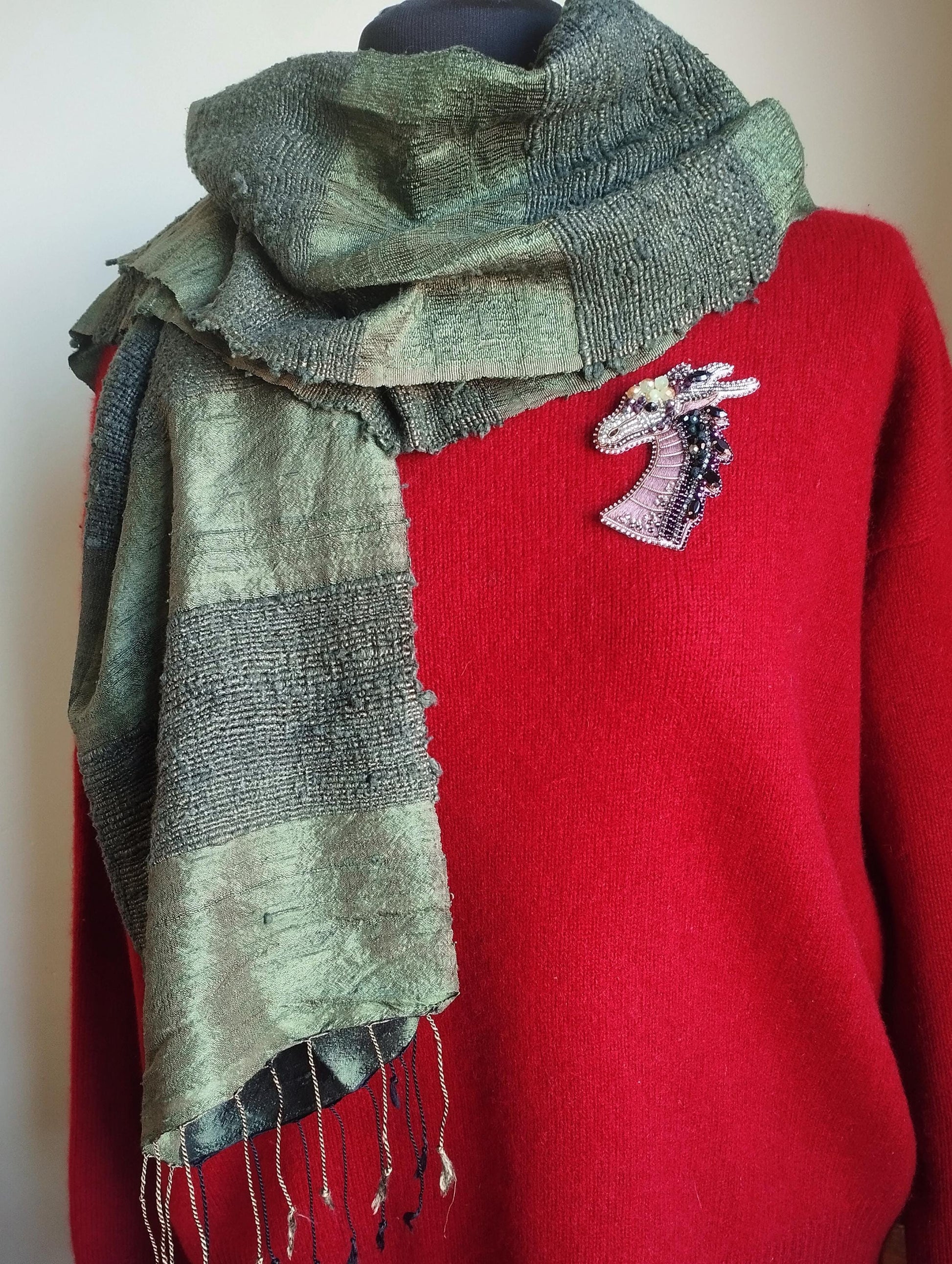 A red sweater with a green and gray scarf draped over it, and a small embroidered giraffe pin on the sweater.