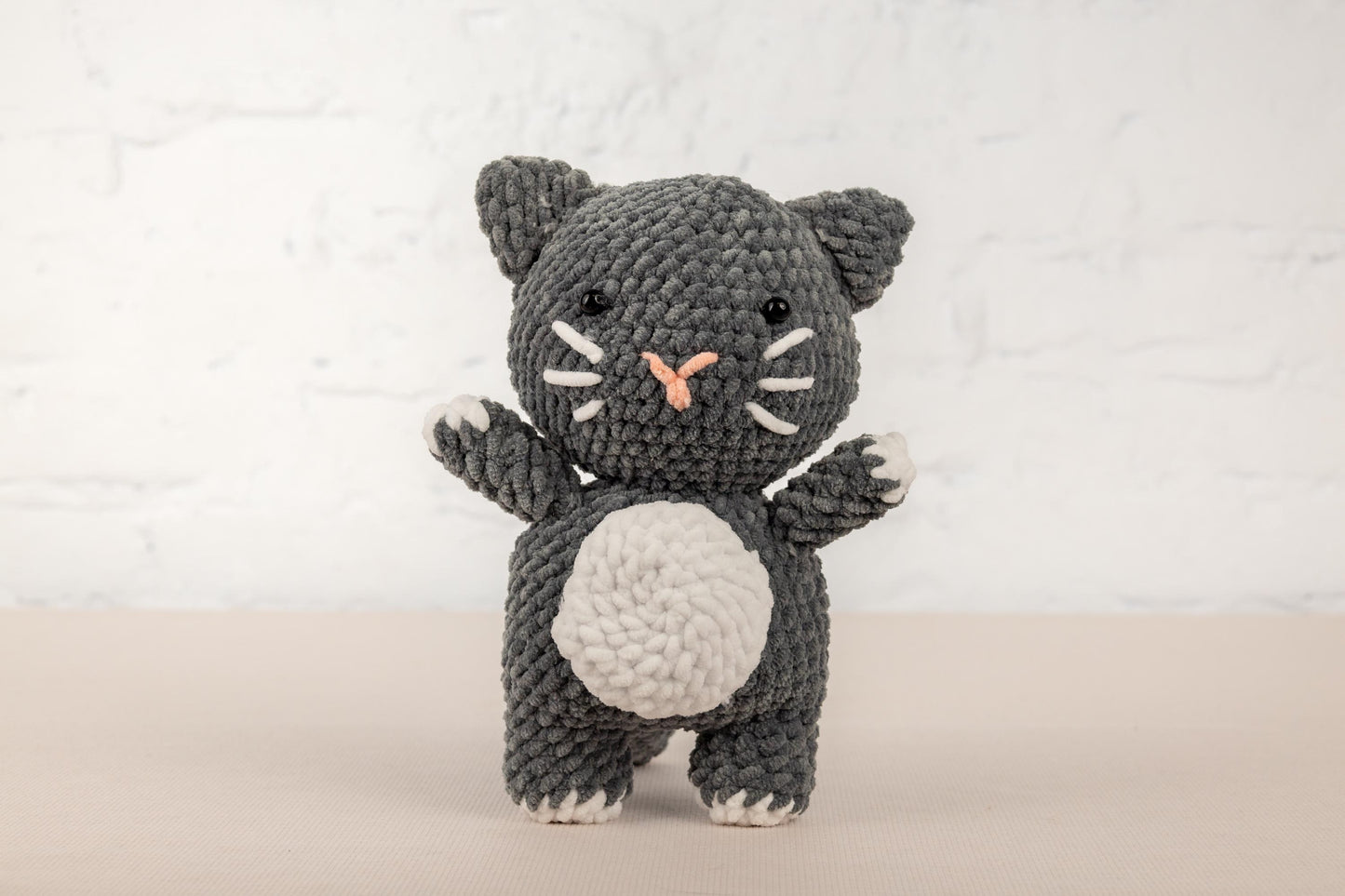 a crocheted black and white cat holding a white ball