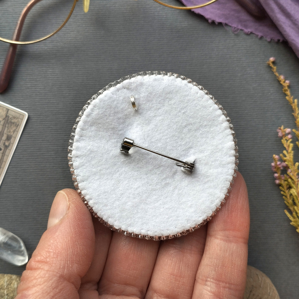 A hand holding a round pin cushion with a pin attached to it.