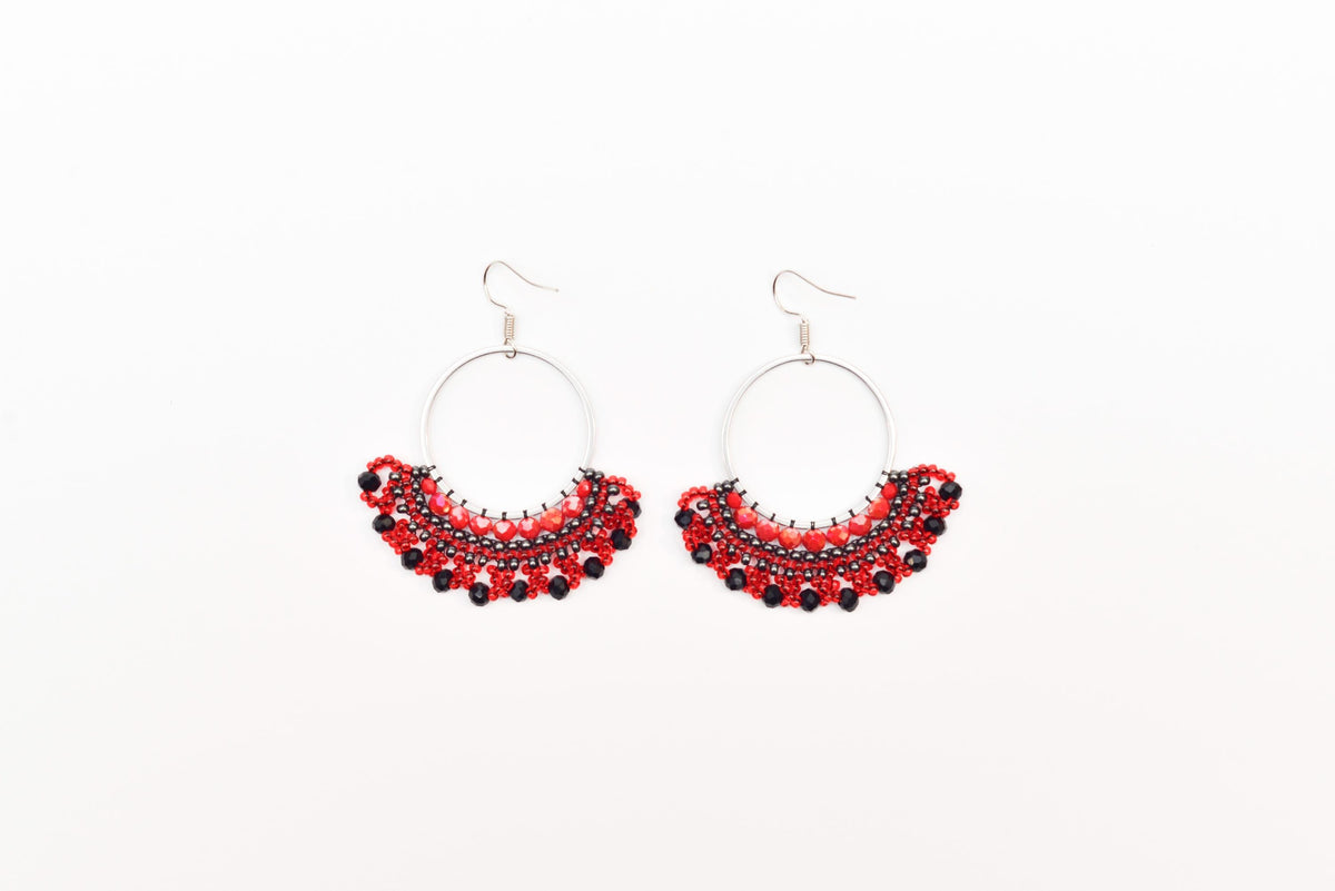 A pair of red and black beaded earrings with circular hooks, displayed against a white background.