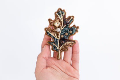 a hand holding a beaded leaf brooch