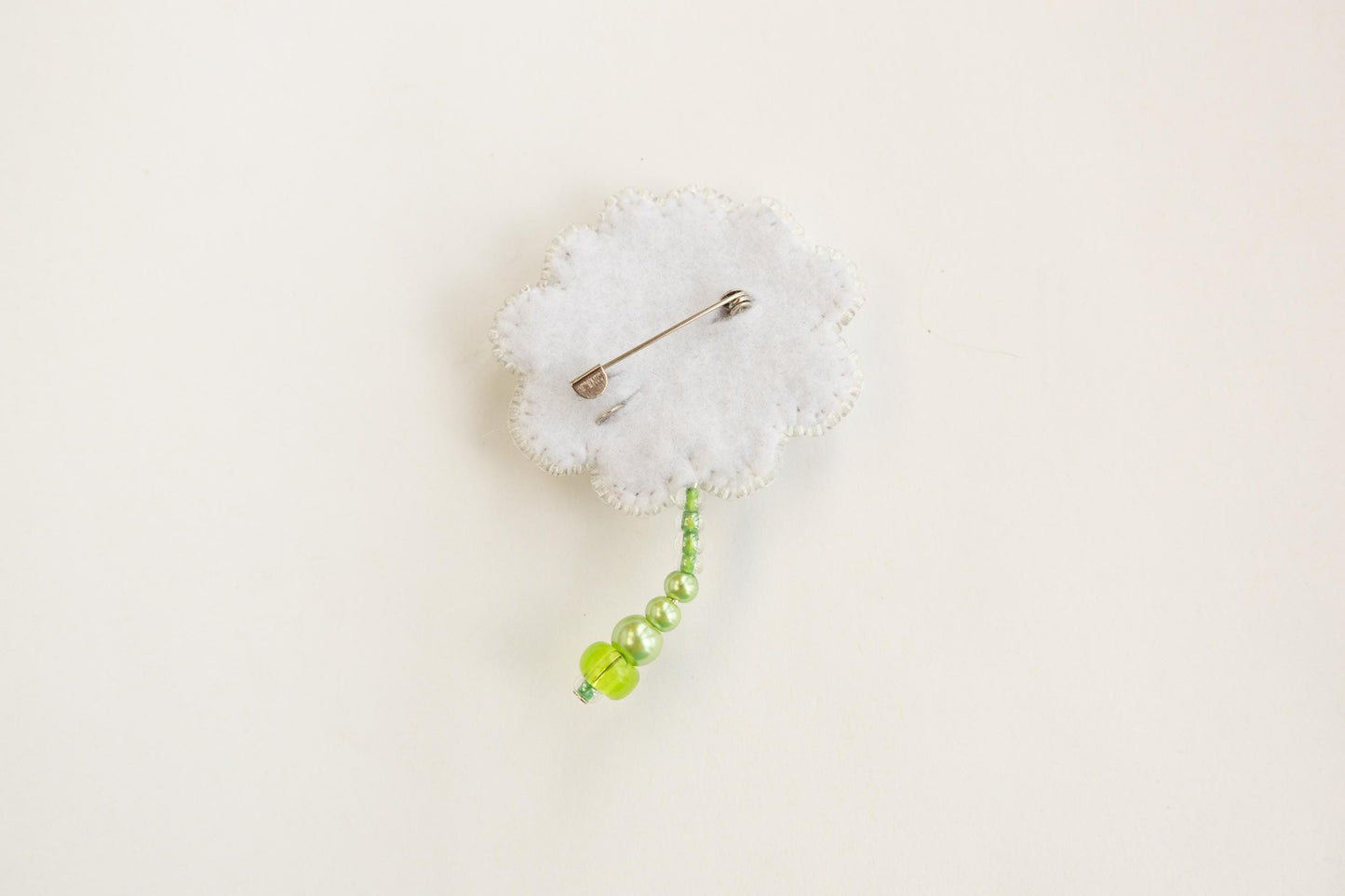 a white cloud shaped brooch with a green bead