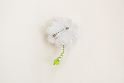 a white cloud shaped brooch with a green bead