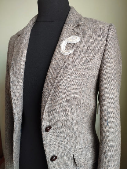 A gray tweed blazer with a white crescent moon pin on the lapel, displayed on a mannequin.