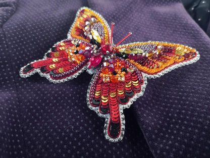 a colorful butterfly brooch sitting on top of a purple cloth