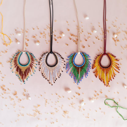 four colorful beaded necklaces with feather-like designs, each with a unique color and pattern, arranged on a pink background with scattered beads.