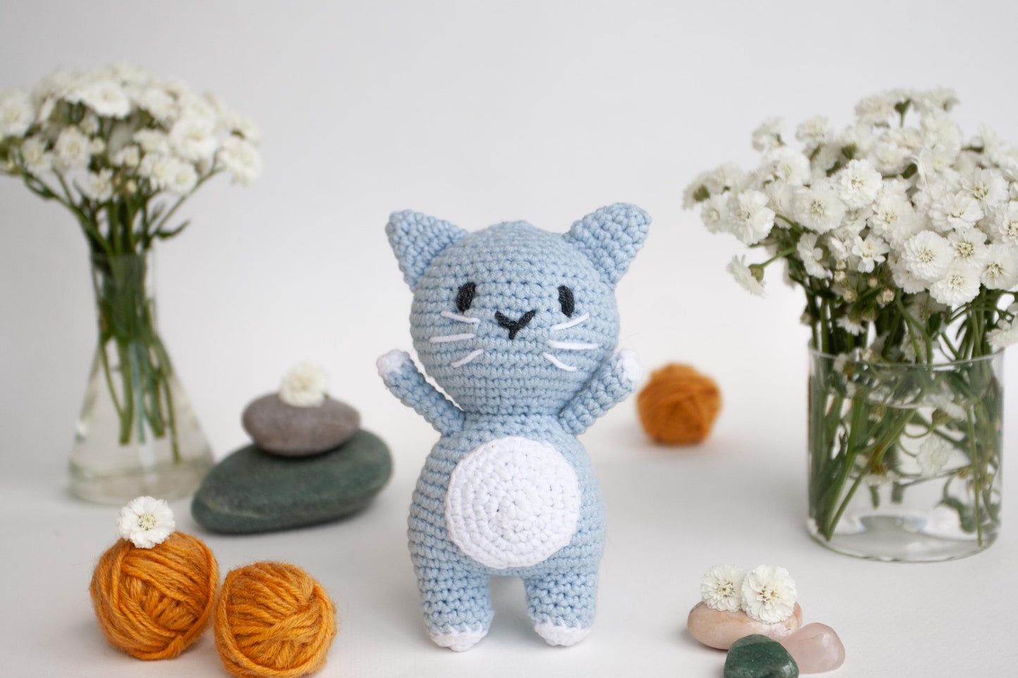 a crocheted cat standing next to a vase of flowers