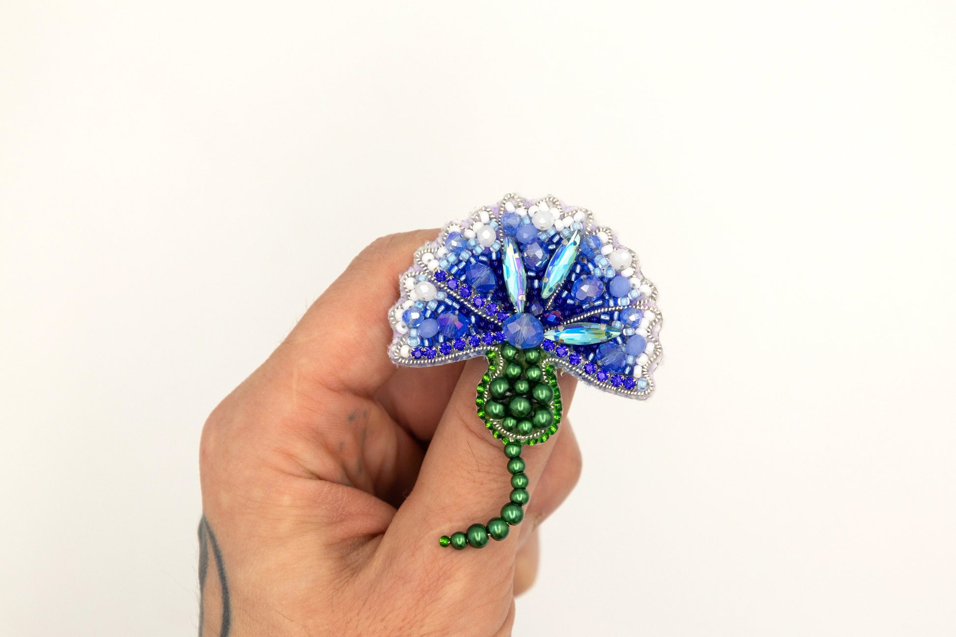 a hand holding a blue and green brooch