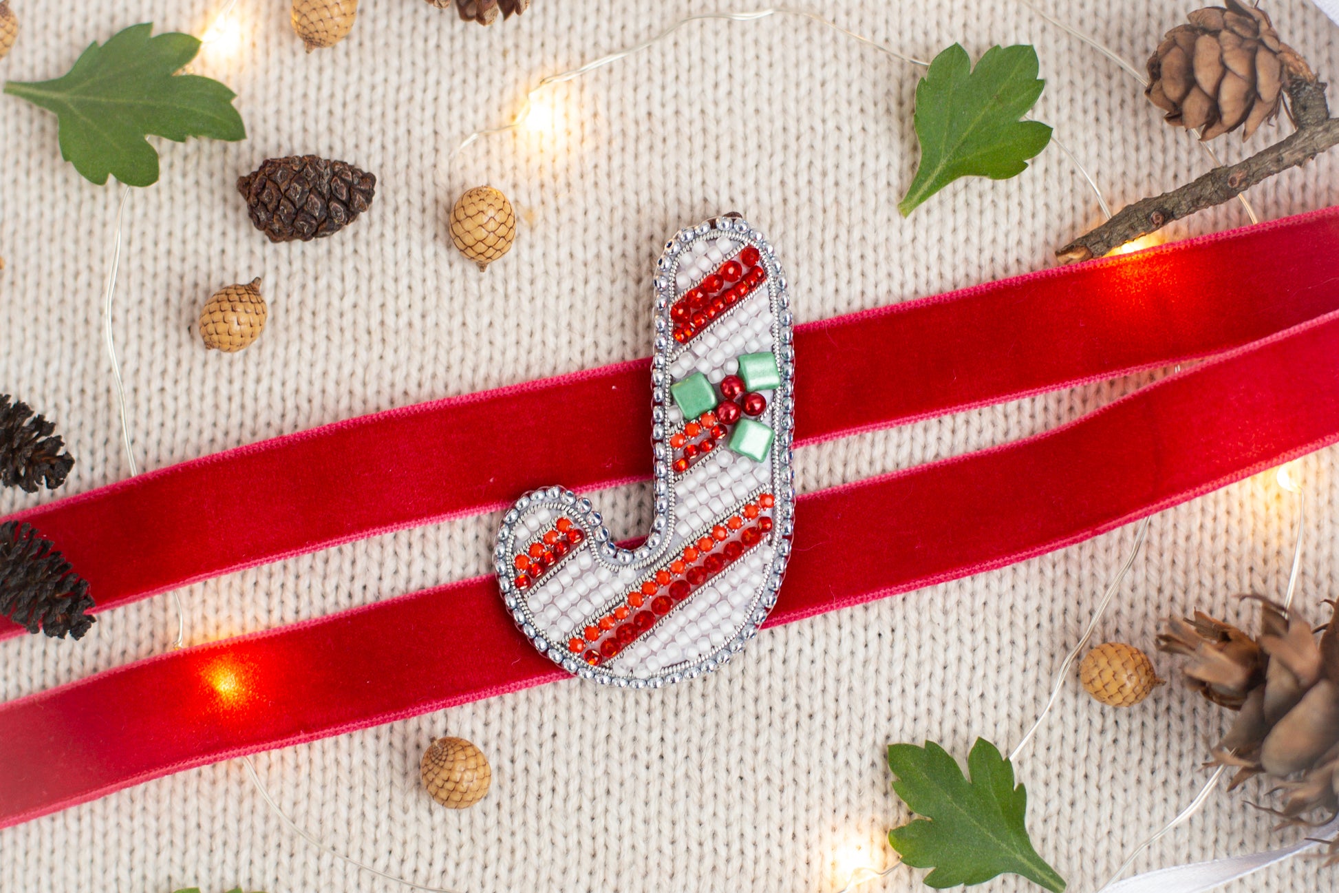 a red ribbon with a decorative letter "J" on it, surrounded by various holiday-themed items such as pine cones, leaves, and other ornaments.