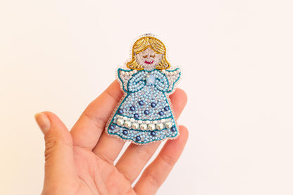 A hand holding a small, intricately beaded figure of a girl with a blue dress and white polka dots.