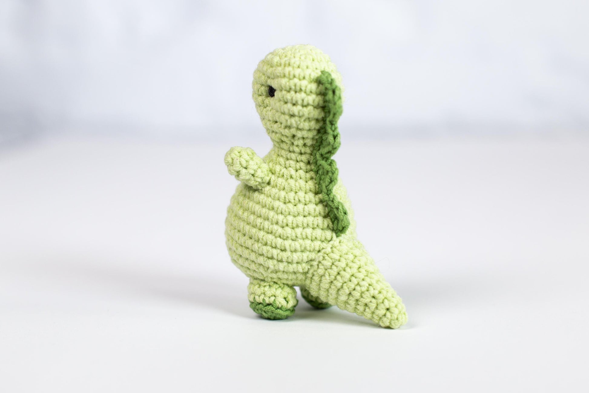 a crocheted green stuffed animal sitting on a white surface