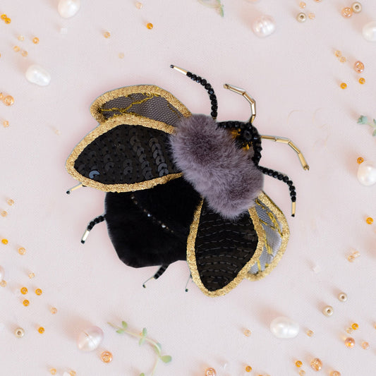 a black and gold bee with a purple fuzzy ball
