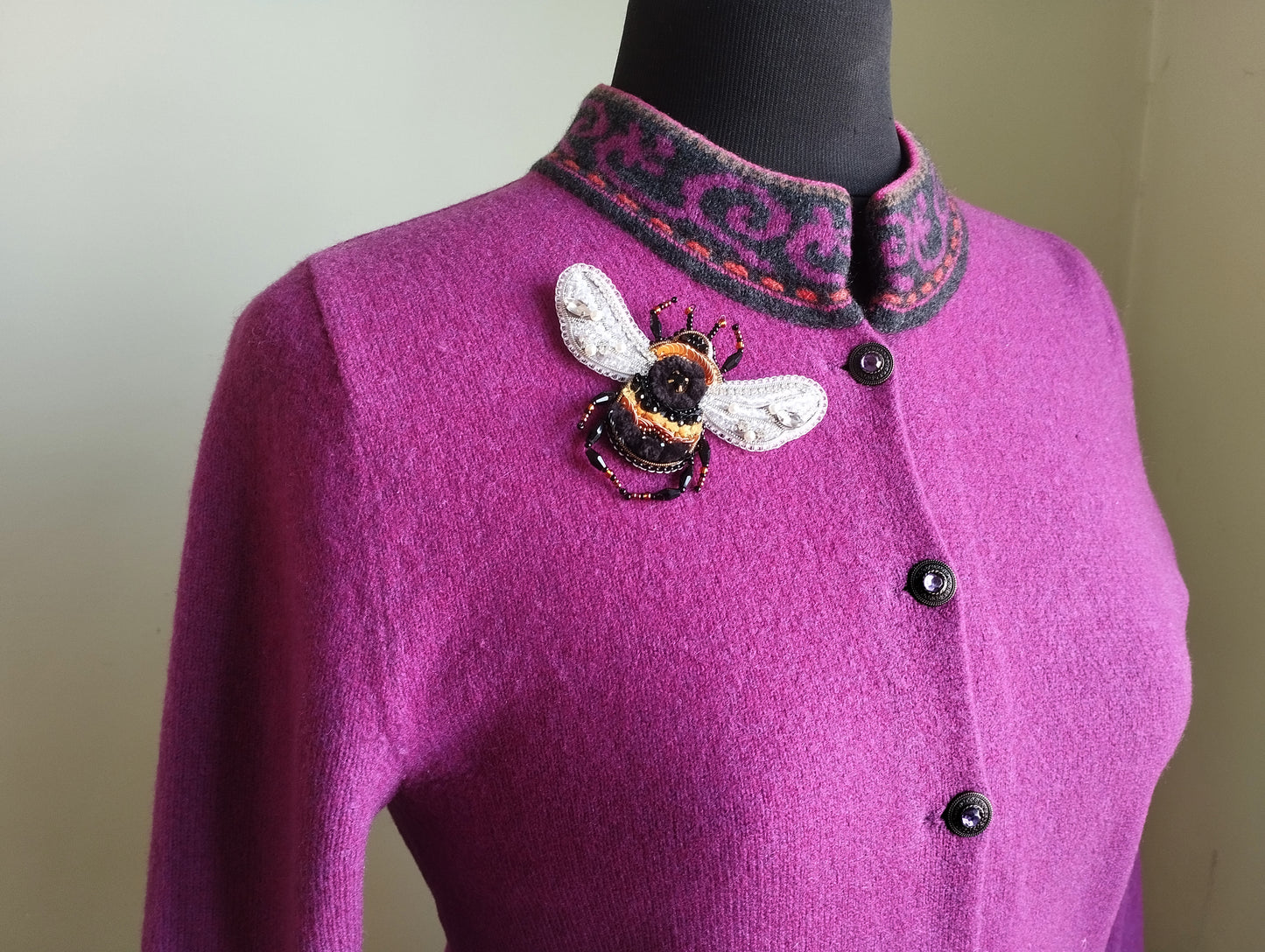 A close-up of a woman wearing a pink cardigan with a decorative bee embroidered on the front.