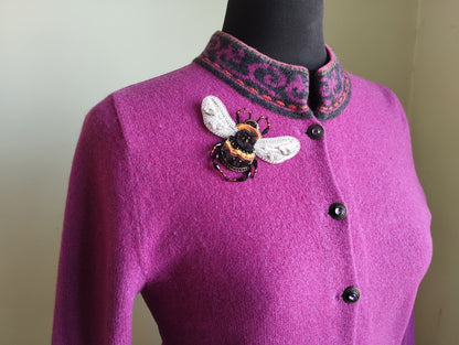A close-up of a woman wearing a pink cardigan with a decorative bee embroidered on the front.