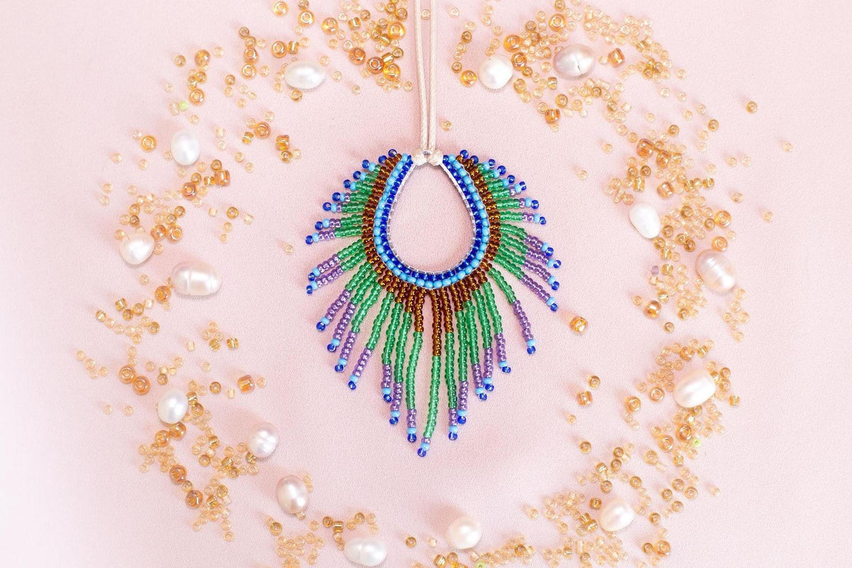 a colorful beaded necklace with a large, eye-catching pendant surrounded by a variety of small, round, and multicolored beads, pearls, and other decorative elements arranged in a circular pattern on a pink background.