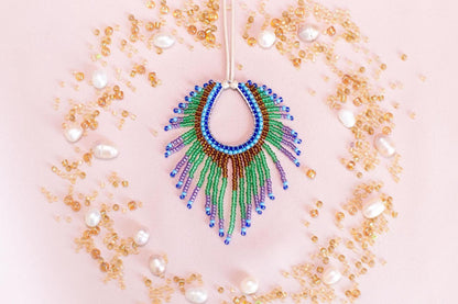 a colorful beaded necklace with a large, eye-catching pendant surrounded by a variety of small, round, and multicolored beads, pearls, and other decorative elements arranged in a circular pattern on a pink background.