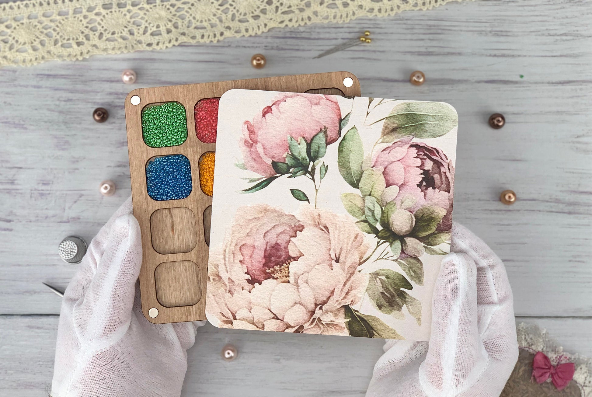 a person in white gloves holding a painting board with flowers on it