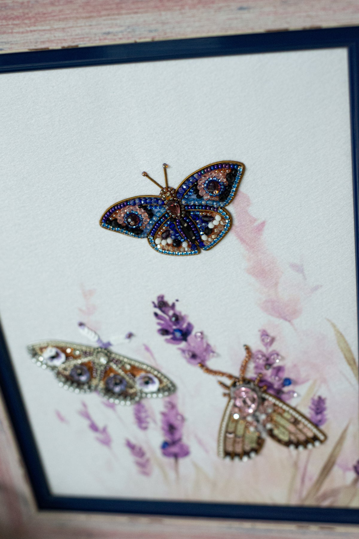 a close-up view of a butterfly with intricate beading and embroidery, set against a background of purple flowers.