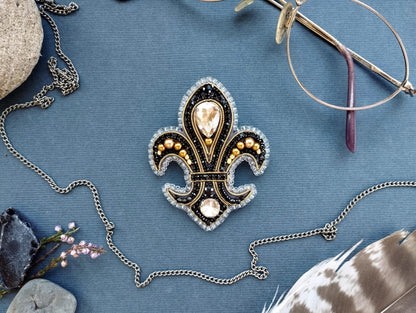 a close-up view of a decorative brooch with a fleur-de-lis design, surrounded by various accessories such as a necklace, glasses, and feathers.