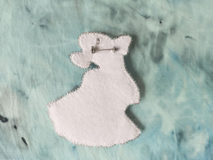 A white felt object resembling a flower or leaf, with a silver pin attached to it, is placed on a textured blue background.