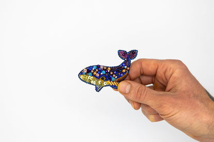 a hand holding a small blue and gold brooch