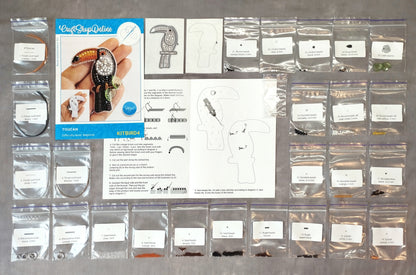 various craft supplies, including a kit for creating a bird-shaped brooch, a blue book with instructions, and several bags containing different materials and tools.