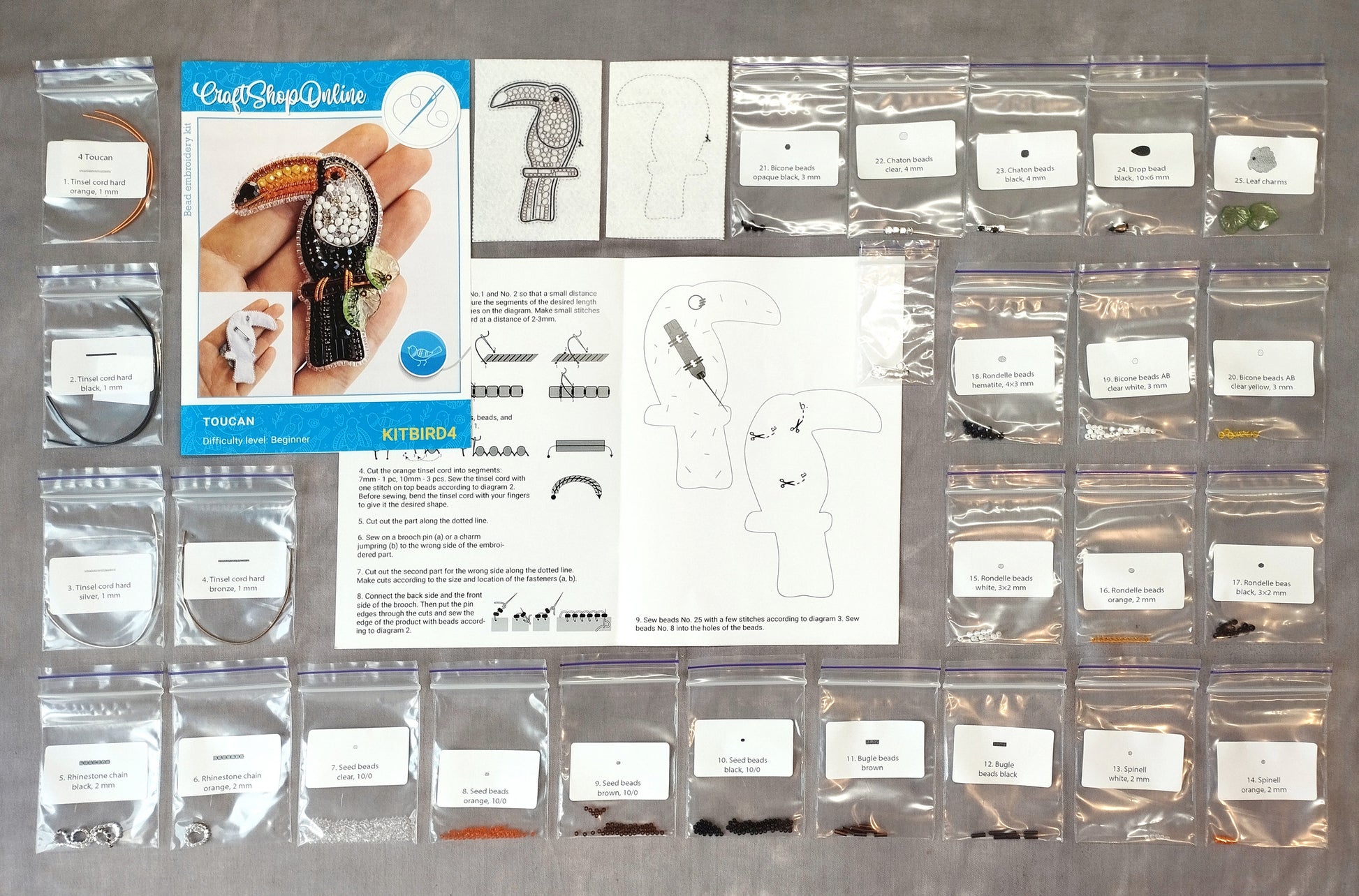 various craft supplies, including a kit for creating a bird-shaped brooch, a blue book with instructions, and several bags containing different materials and tools.