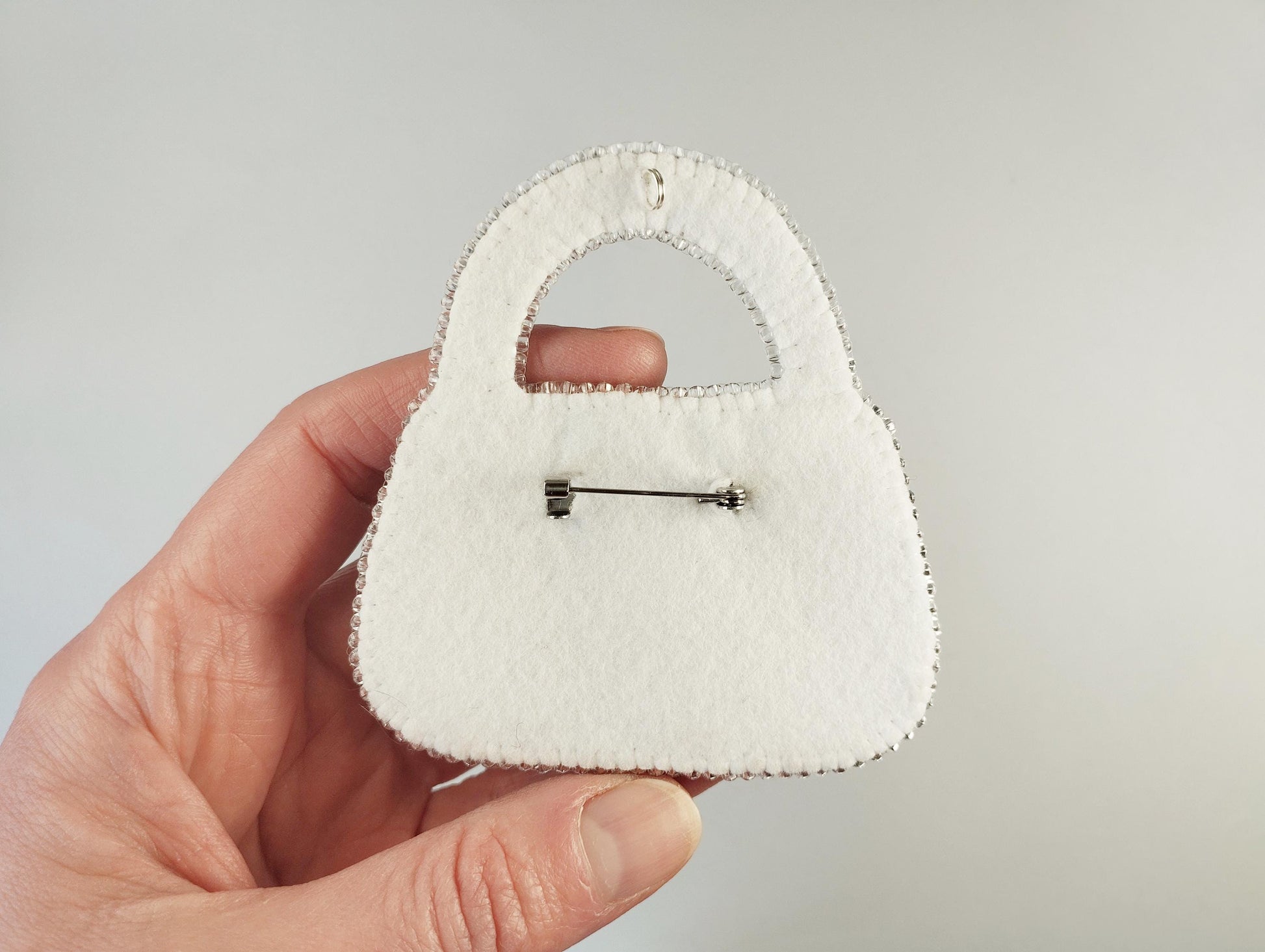 A hand holding a white felt purse with a pin attached to it.