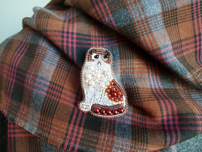 A decorative cat brooch made of beads and pearls is displayed on a plaid fabric background.
