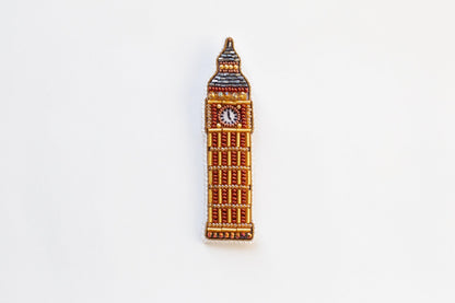 a brooch with a clock on it on a white surface