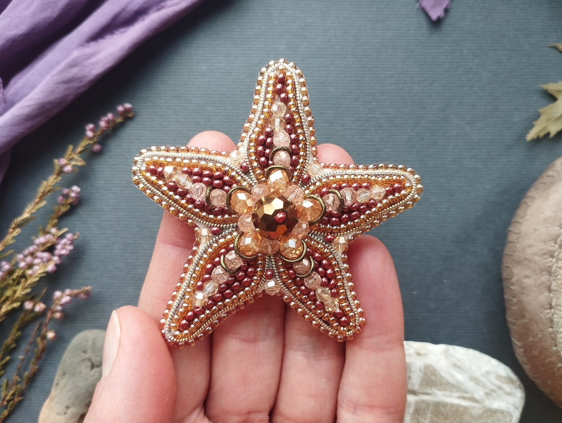 A hand holding a decorative beaded starfish against a dark background.