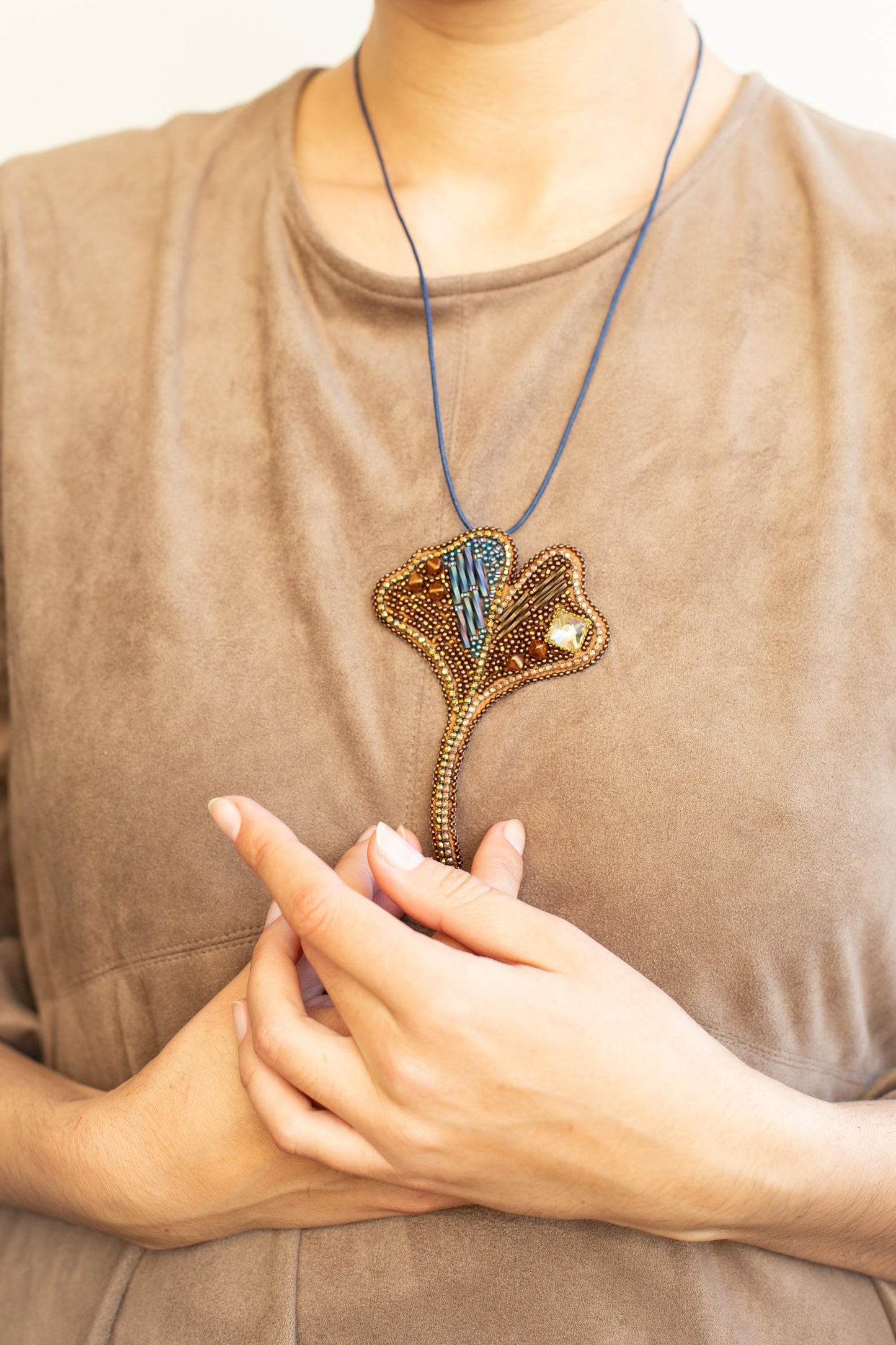 A close-up of a person&#39;s hands wearing a beige shirt, with a necklace featuring a decorative pendant.