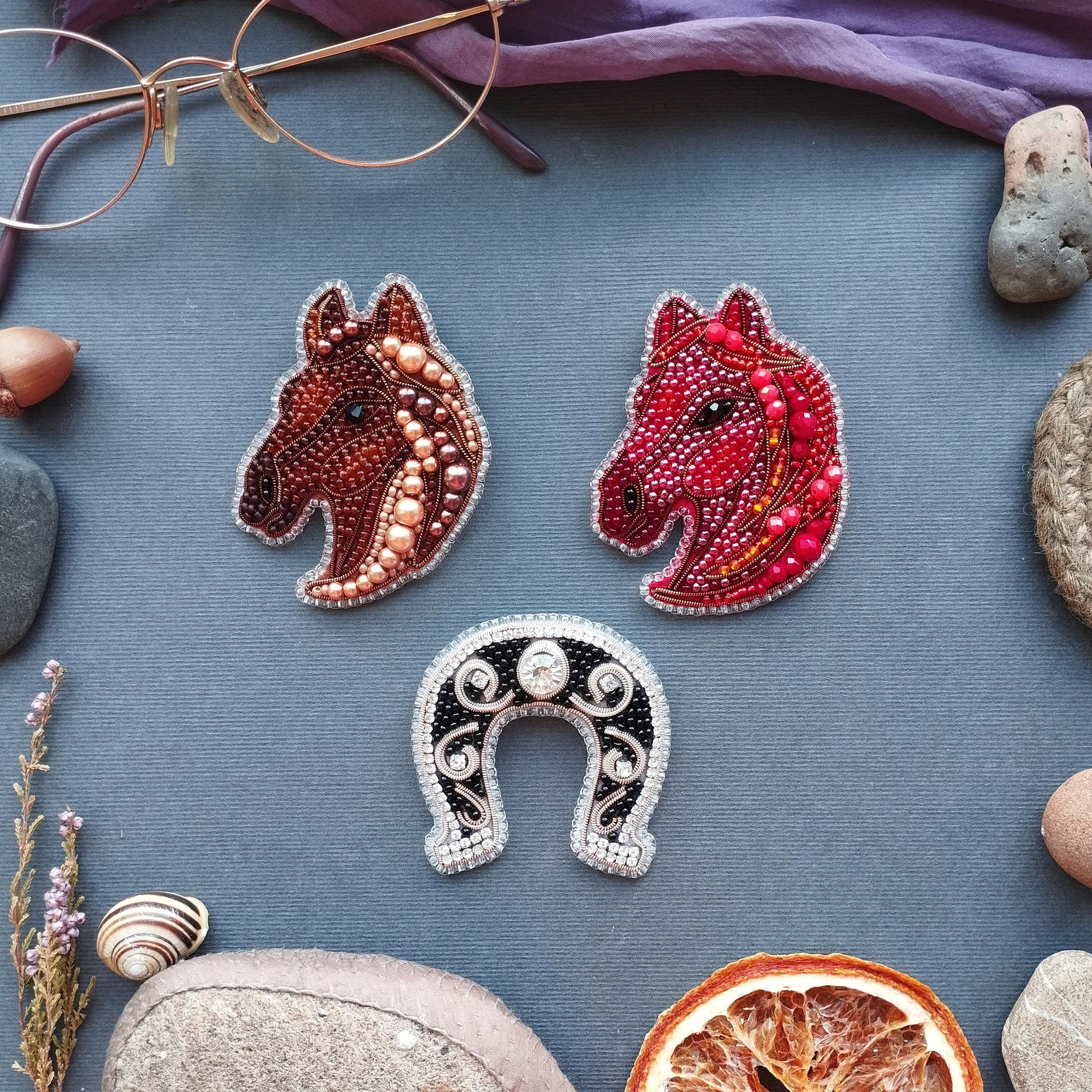 three decorative horse-shaped brooches, a horseshoe, and various natural elements such as rocks, a grapefruit, and a pair of glasses.