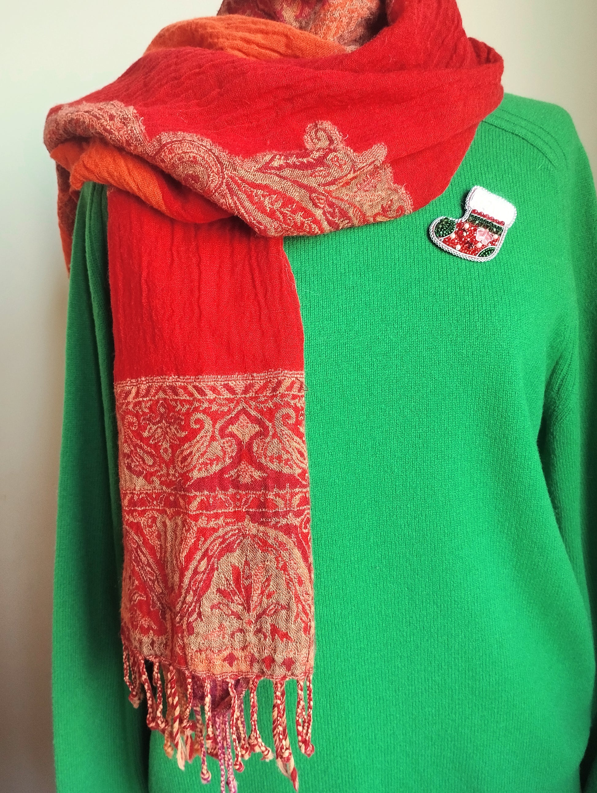 A person wearing a green sweater and a red and gold patterned scarf.