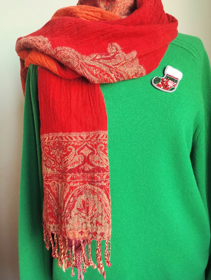 A person wearing a green sweater and a red and gold patterned scarf.