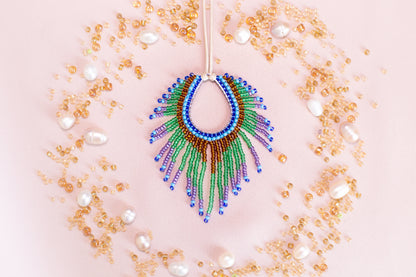 a colorful beaded necklace with a large, eye-catching pendant surrounded by a variety of small, round, and multicolored beads, pearls, and other decorative elements arranged in a circular pattern on a pink background.