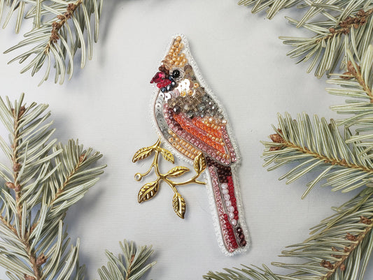 a beaded bird ornament hanging from a pine branch