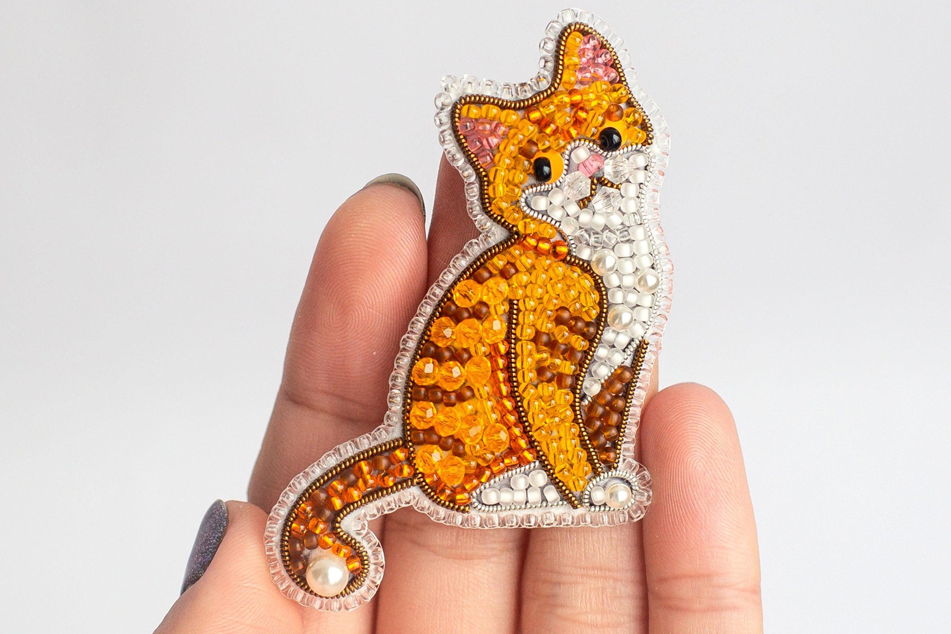 A hand holding a decorative beaded cat pin.