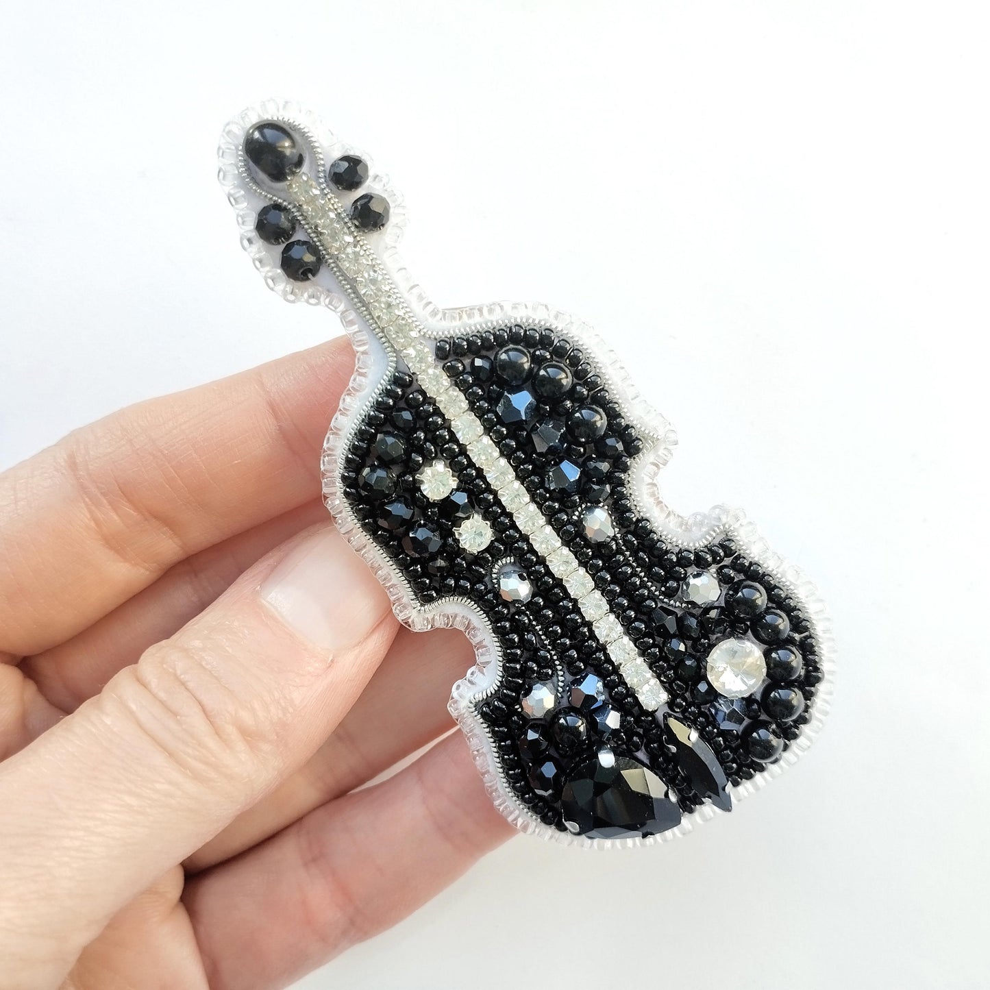 A hand holding a decorative piece of jewelry, which appears to be a brooch or pin, featuring a black and white design with numerous small beads or stones.