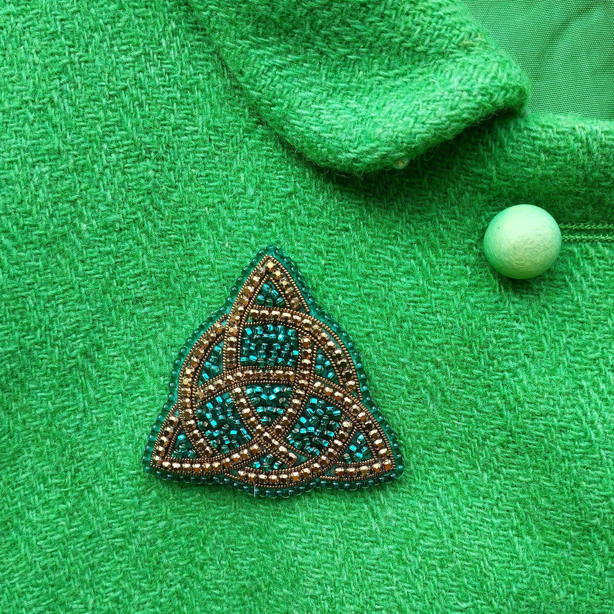 a close-up view of a green fabric with a triangular beaded piece of jewelry, possibly a brooch, placed on it.